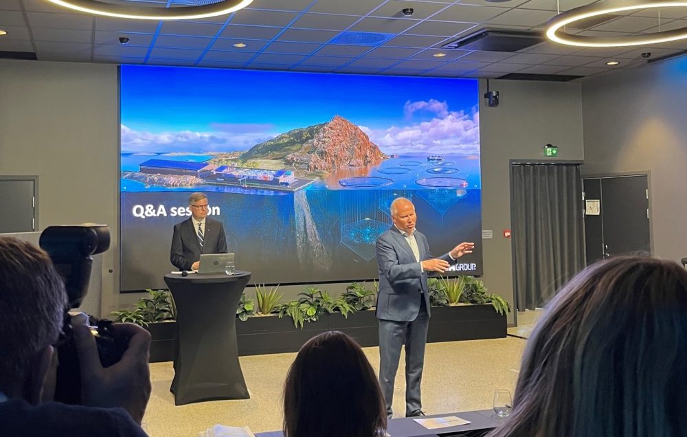 Speakers at AKVA Capital Markets Day in front of a large screen, with projections of fish farms in the background