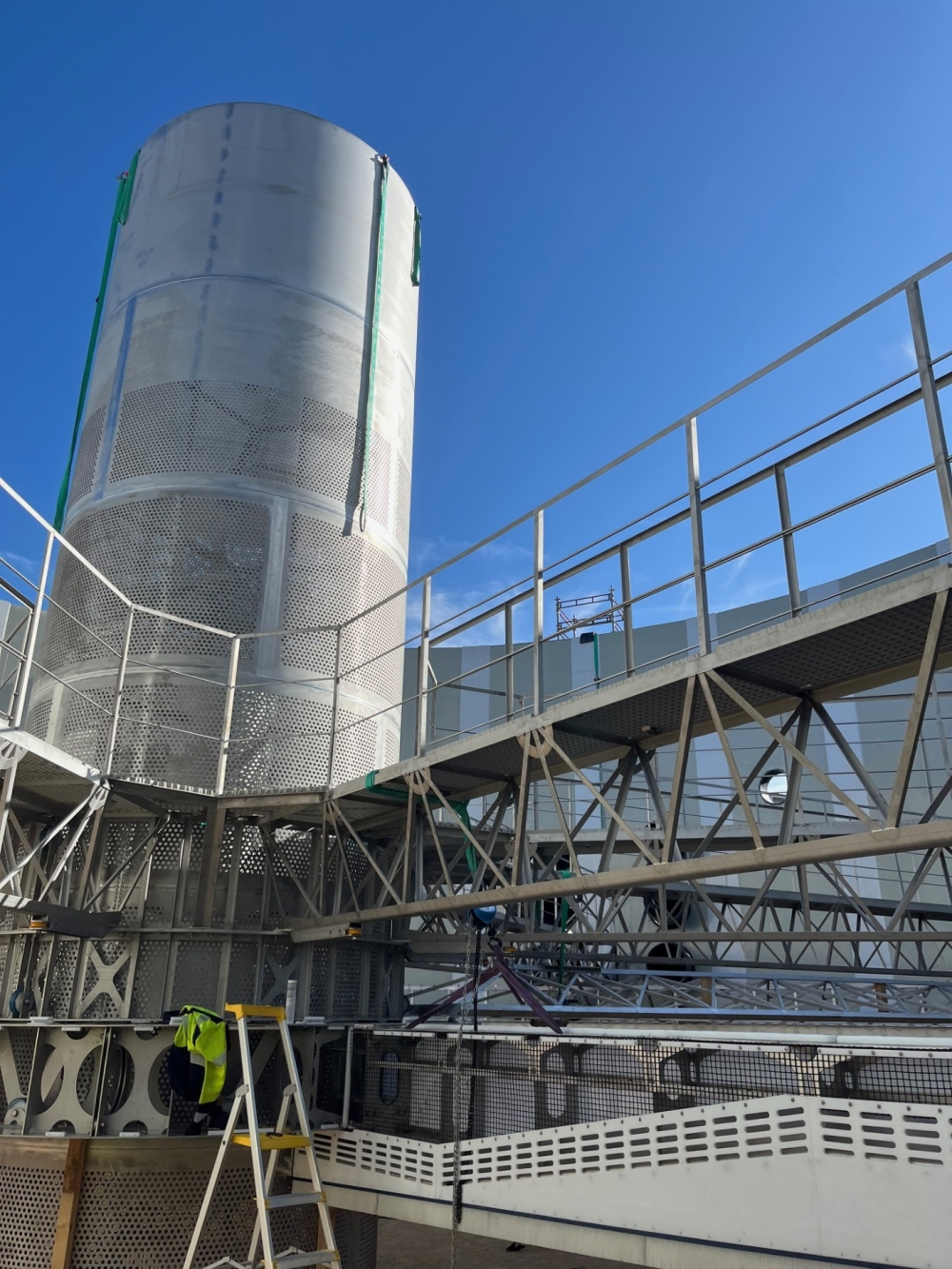 Interior view of a large metallic tank and industrial structures under assembly at an aquaculture facility, with visible platforms and scaffolding under clear blue skies.
