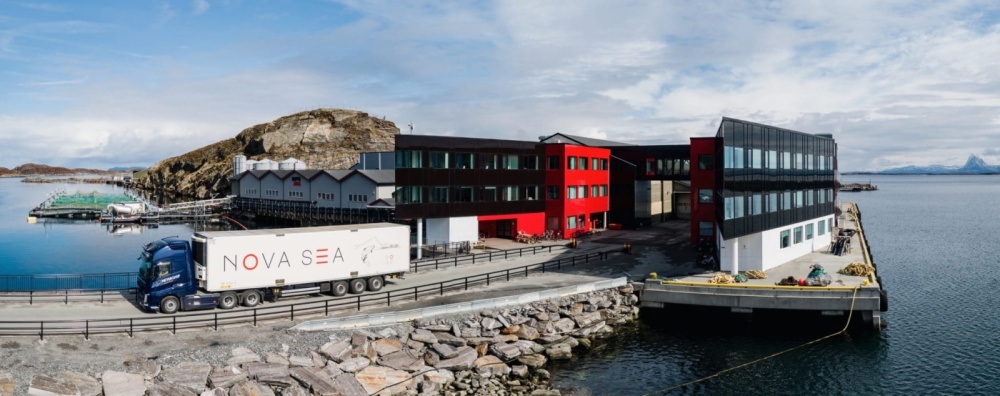 Hauptsitz und Produktionsanlage von Nova Sea an der norwegischen Küste mit modernen roten und schwarzen Gebäuden direkt am Meer, Fischfarmen und einem Transportfahrzeug im Vordergrund.